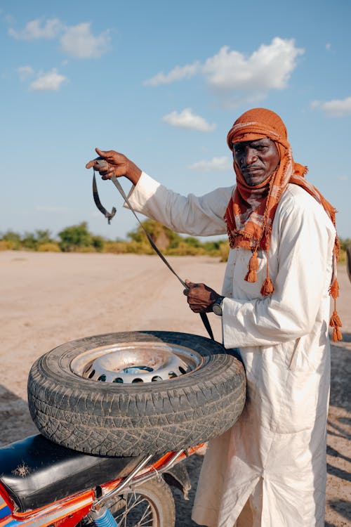 Man in Traditional Clothing Standing by Motorbike Wheel