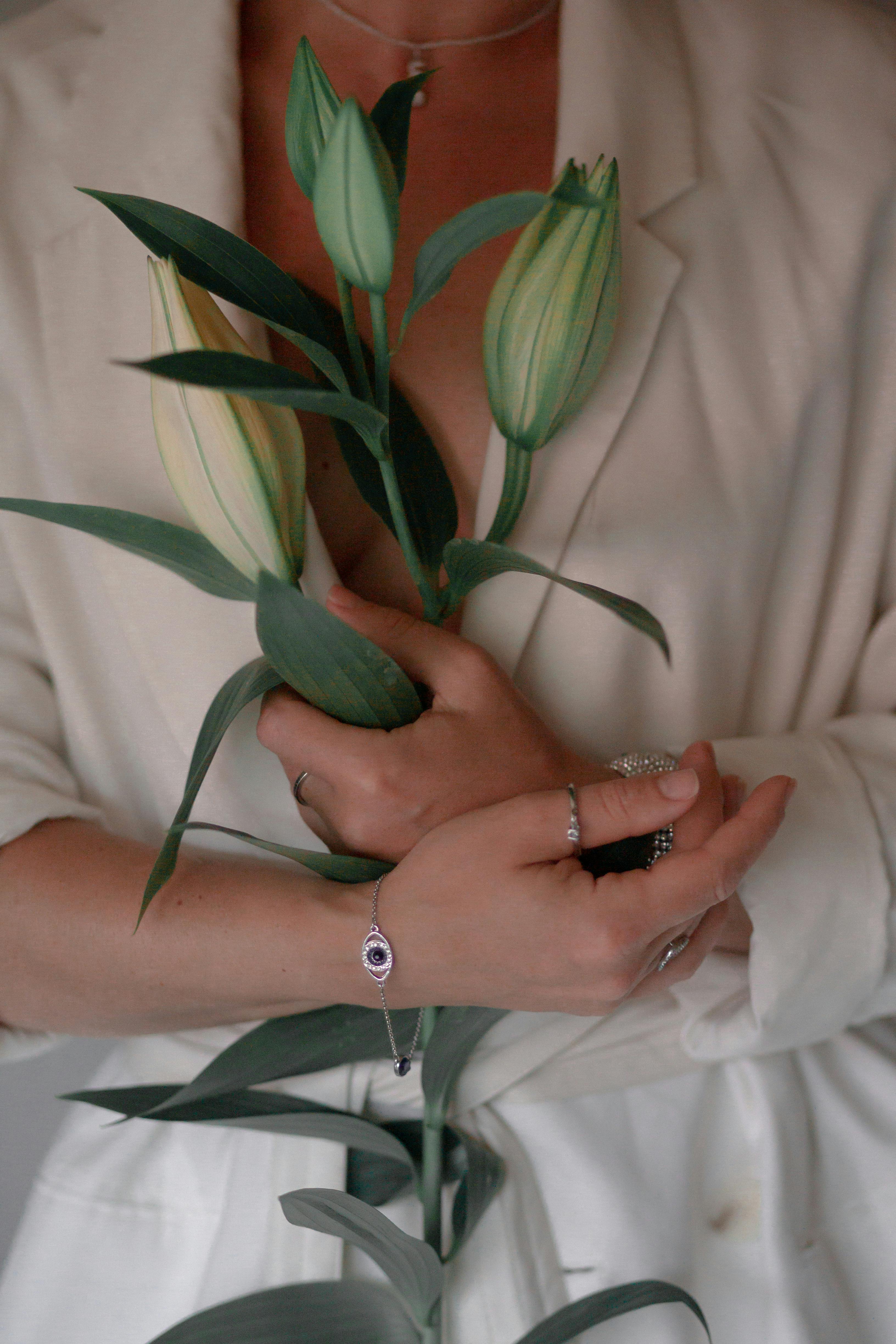 A close-up of a woman's hands elegantly holding white lily buds, showcasing rings and bracelets.