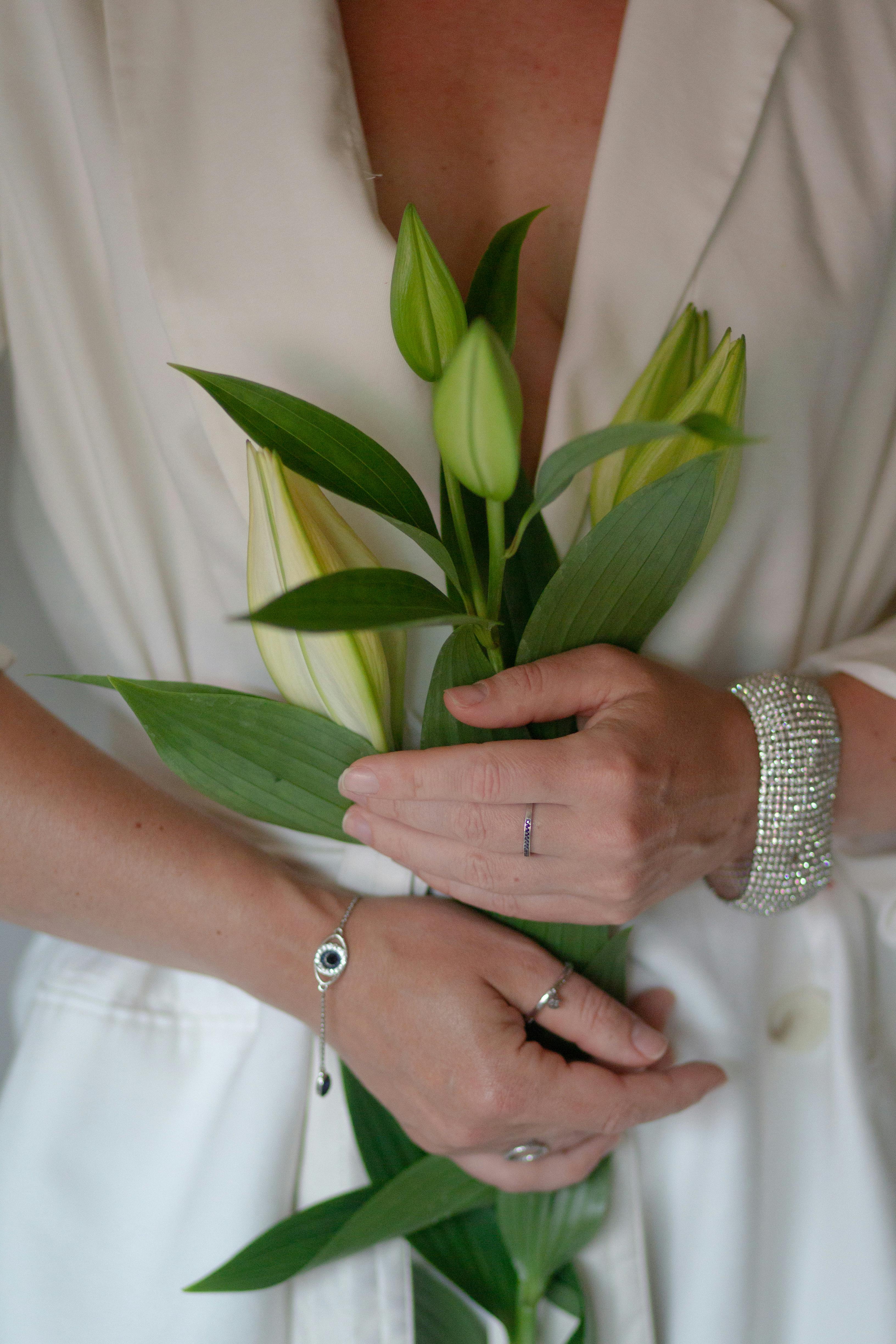 Elegant shot of a woman in a white dress holding lily flowers, showcasing jewelry.