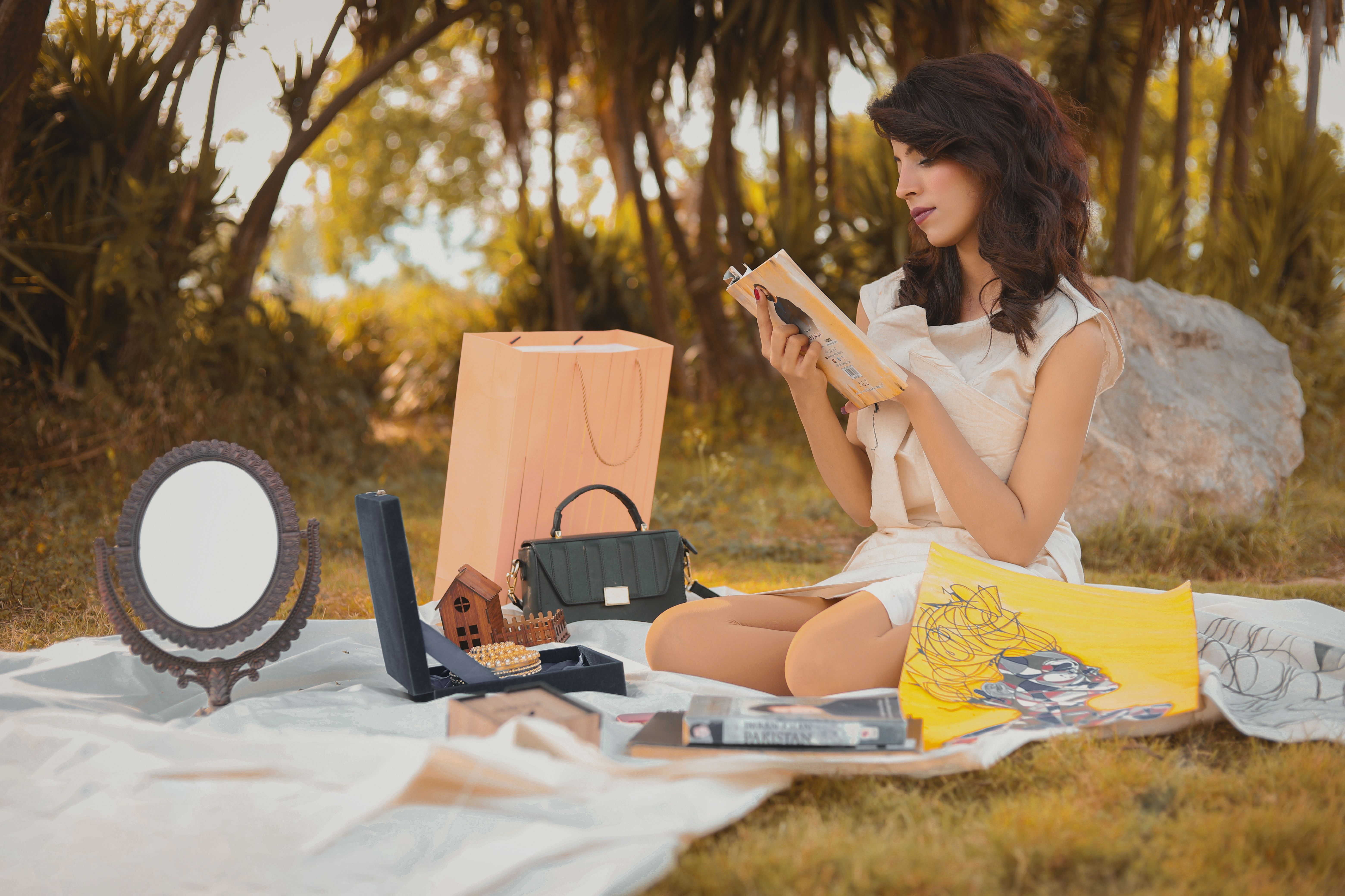 A fashion model enjoys a relaxing moment outdoors in Islamabad, reading and surrounded by accessories.