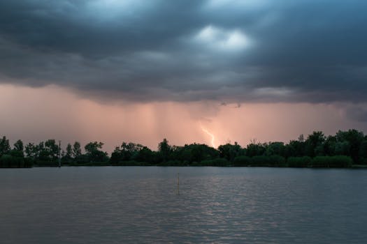 A stunning scene of a thunderstorm with lightning striking over a calm lake and forest.