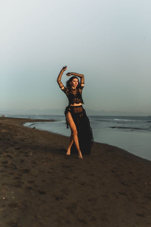 Free Woman in a black dress posing elegantly on a beach at sunset. Stock Photo