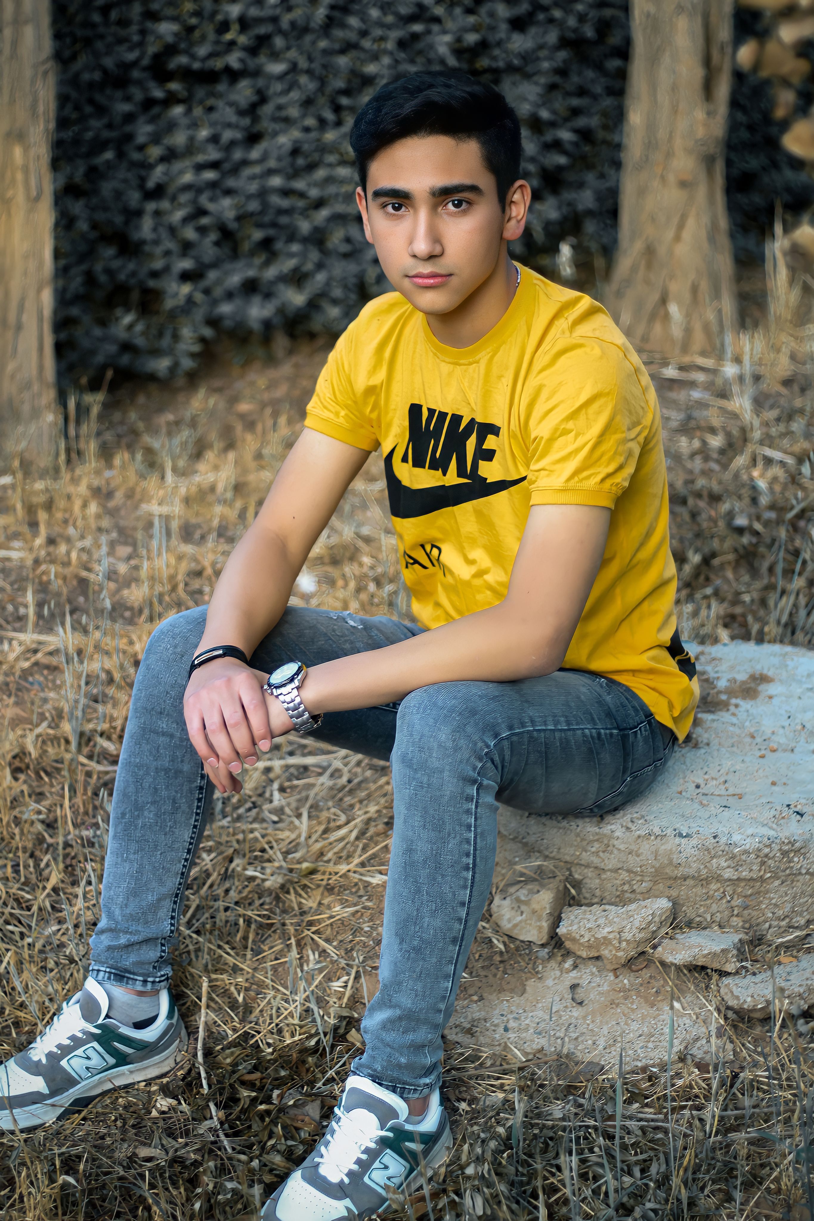 Teenager sitting on a rock outdoors, wearing a yellow t-shirt and jeans.