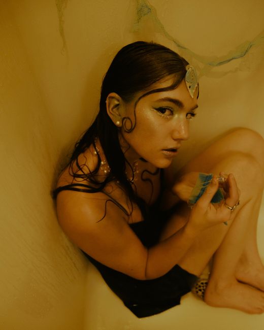 Artistic portrait of a woman with makeup holding a crystal in a bathtub setting.