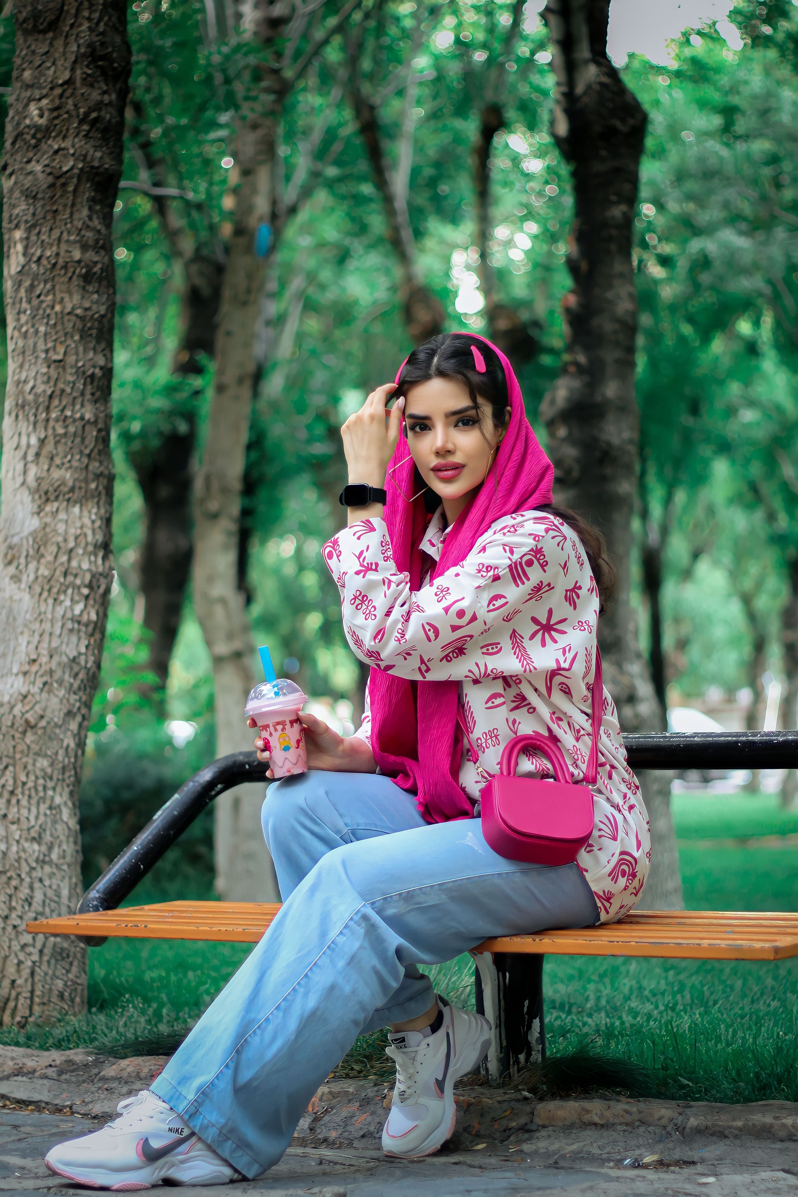 Fashionable woman in park with pink accessories and drink, enjoying summer day.