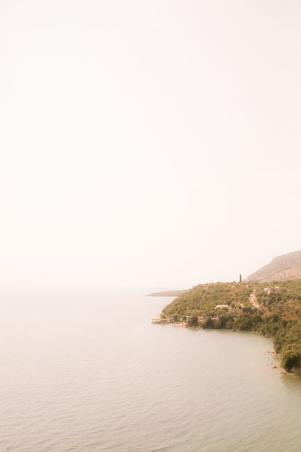 A peaceful aerial view of a coastline with lush greenery and calm waters under a hazy sky.
