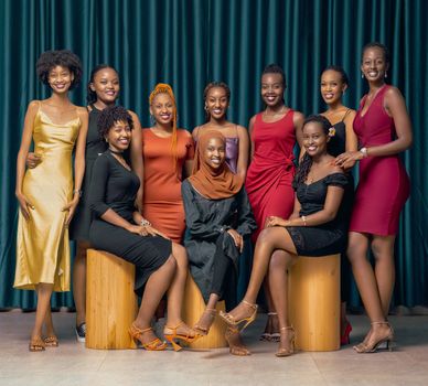 Elegant group portrait of smiling women in colorful dresses against a teal curtain backdrop.