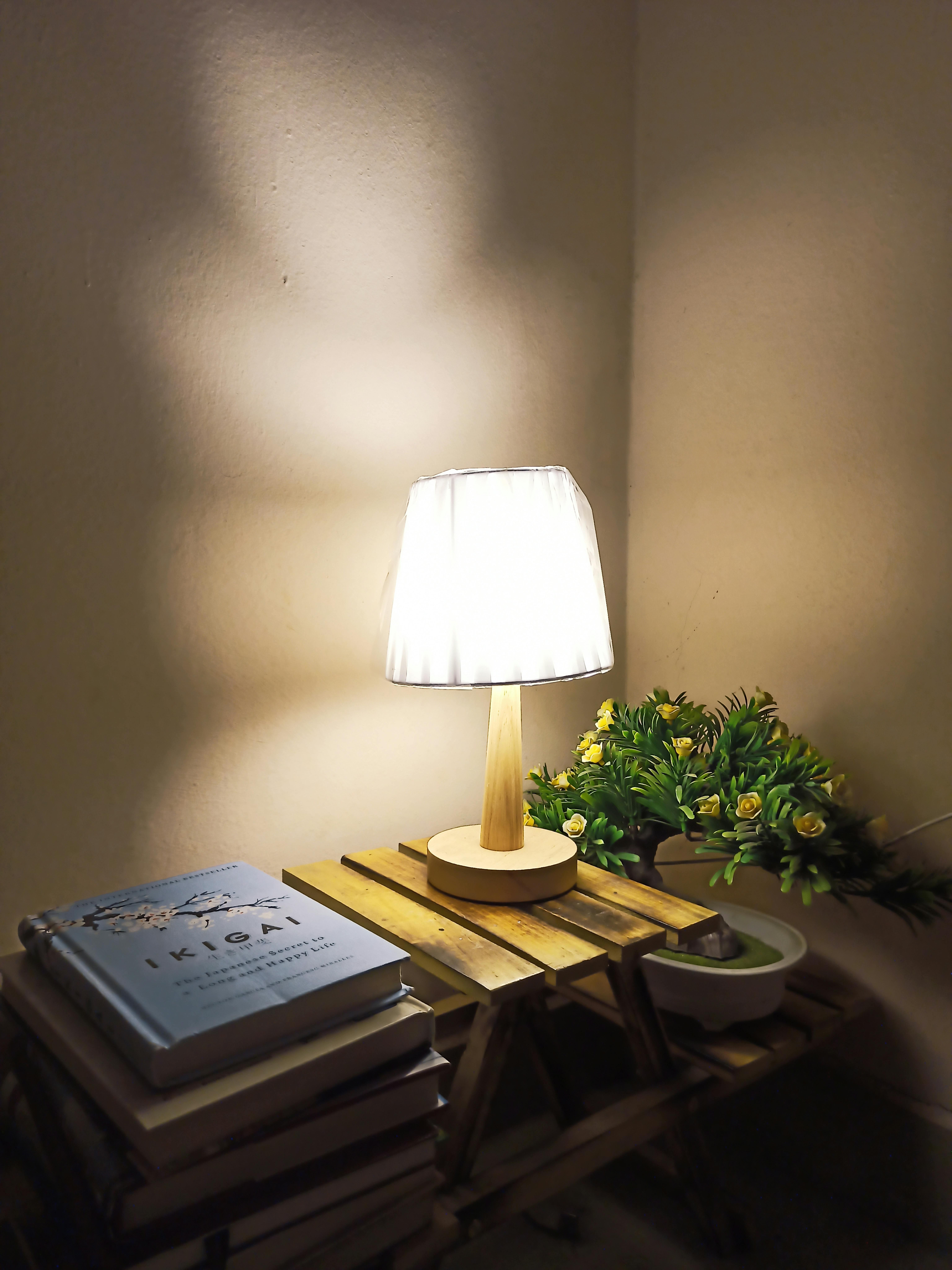Free Warm and inviting corner with a lamp and books on a wooden nightstand. Stock Photo
