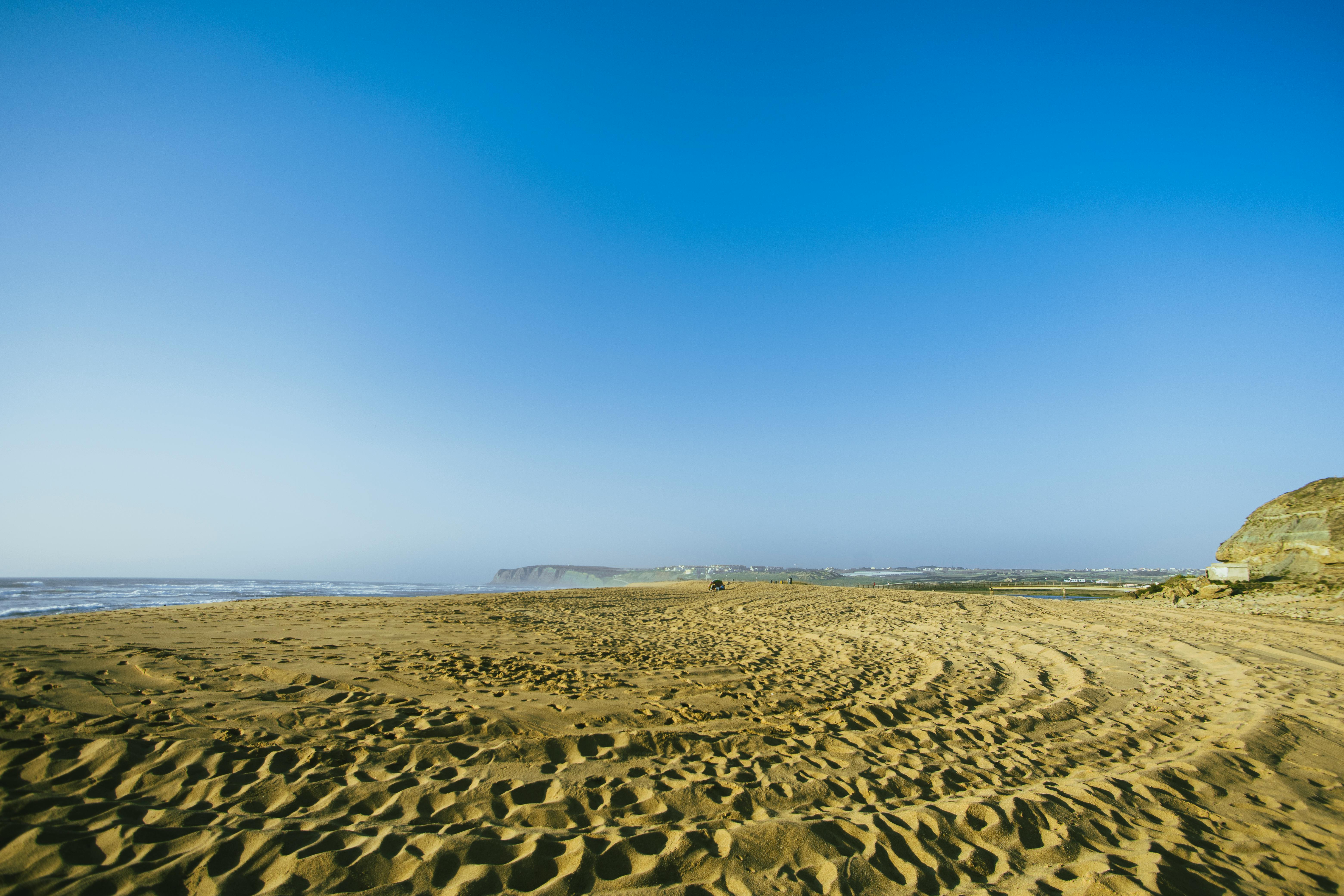 A peaceful sandy beach under a clear blue sky with gentle ocean waves, ideal for relaxation.