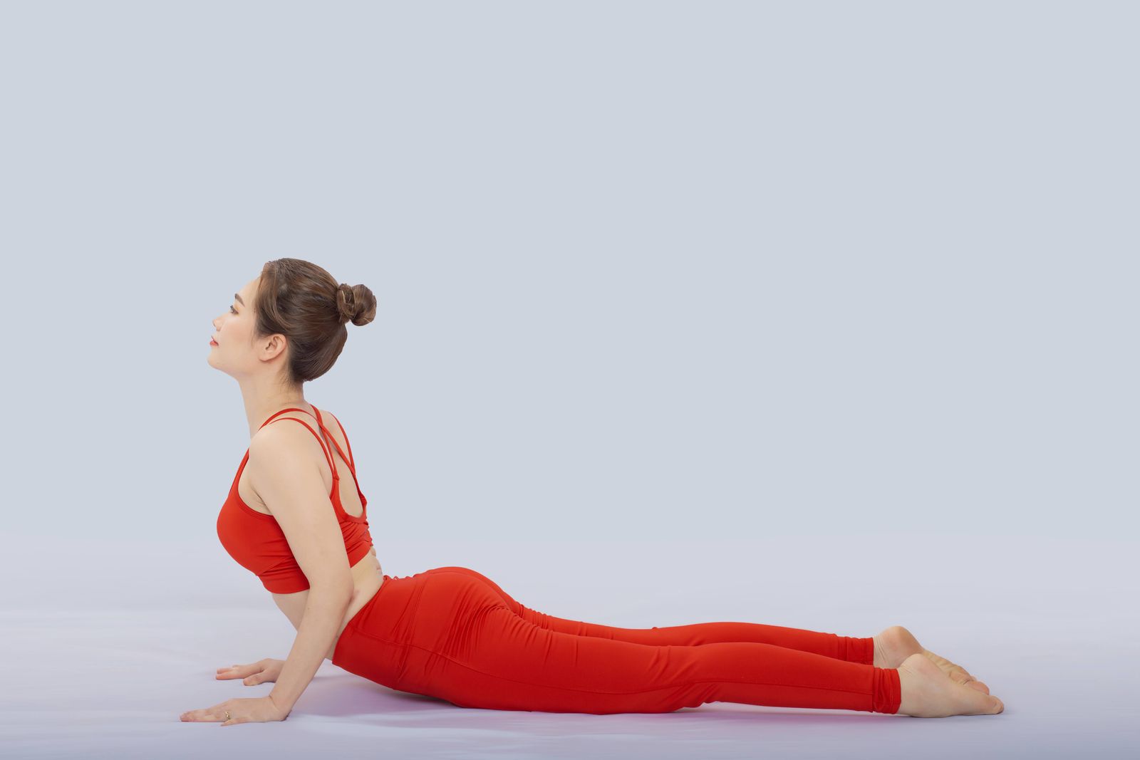 Woman in vibrant red sportswear performing bhujangasana cobra pose in a yoga studio
