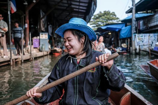 Happy woman rowing a boat at a vibrant floating market in Bangkok, Thailand.