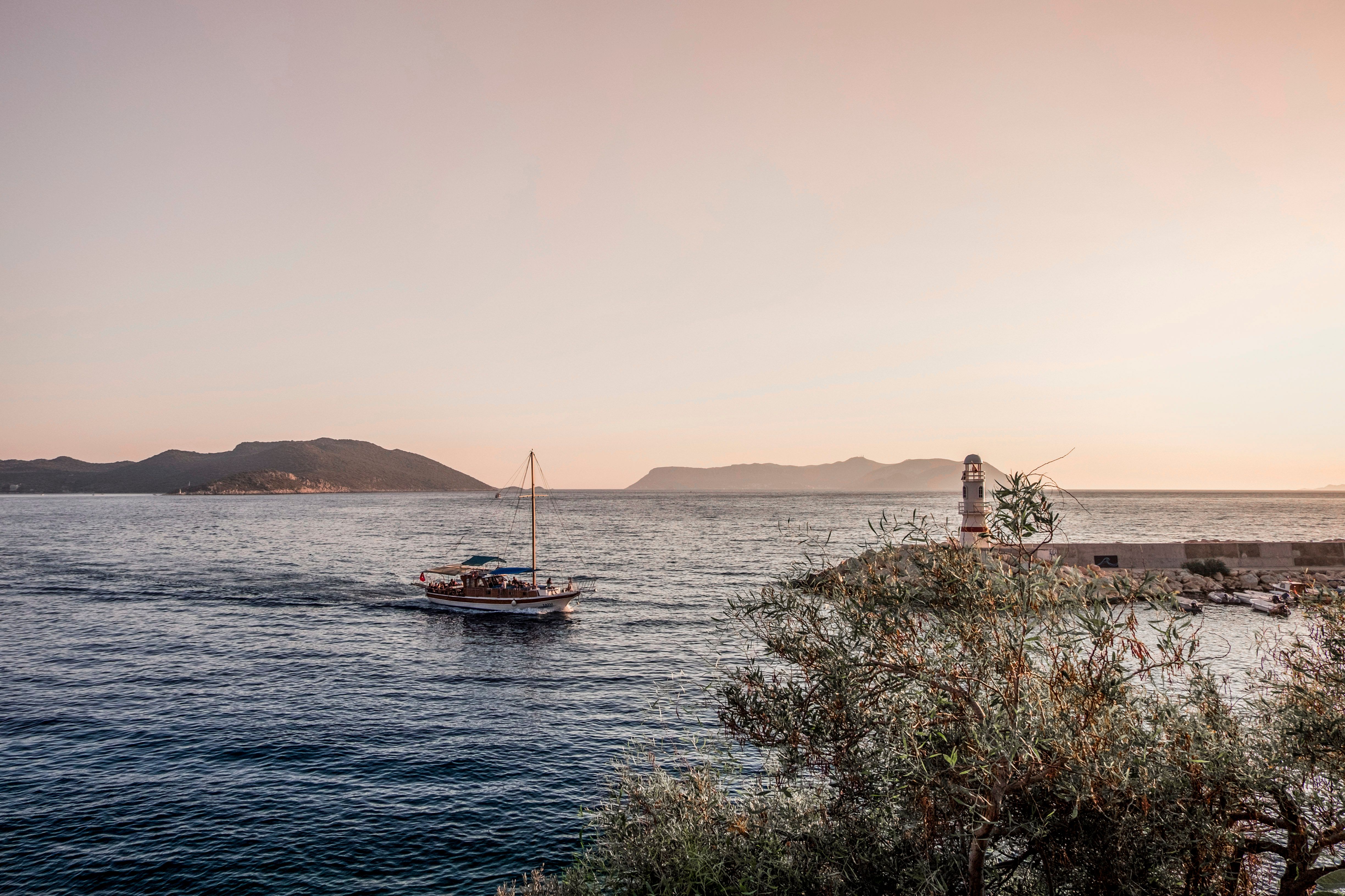 A tranquil scene of a boat sailing at sunset near Kaş, Türkiye, with mountains in the background.