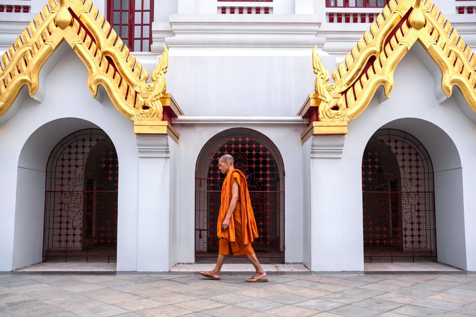 A Buddhist monk walks past the ornate architecture of Loha Prasat Temple in Bangkok, Thailand.