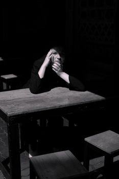Moody black and white portrait of a woman at a table, capturing contemplative solitude.