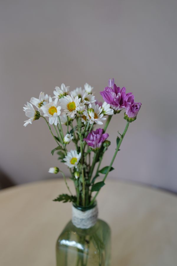 Um charmoso buquê de margaridas e flores roxas exibido em um vaso de vidro verde sobre a mesa.