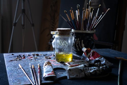 Paint Tubes and Paintbrushes in a Cup Standing on a Table 