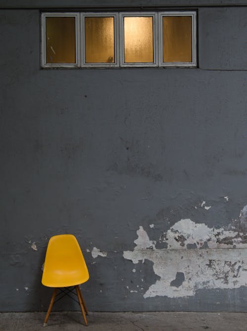 A Yellow Chair Standing by a Wall with Peeling Paint