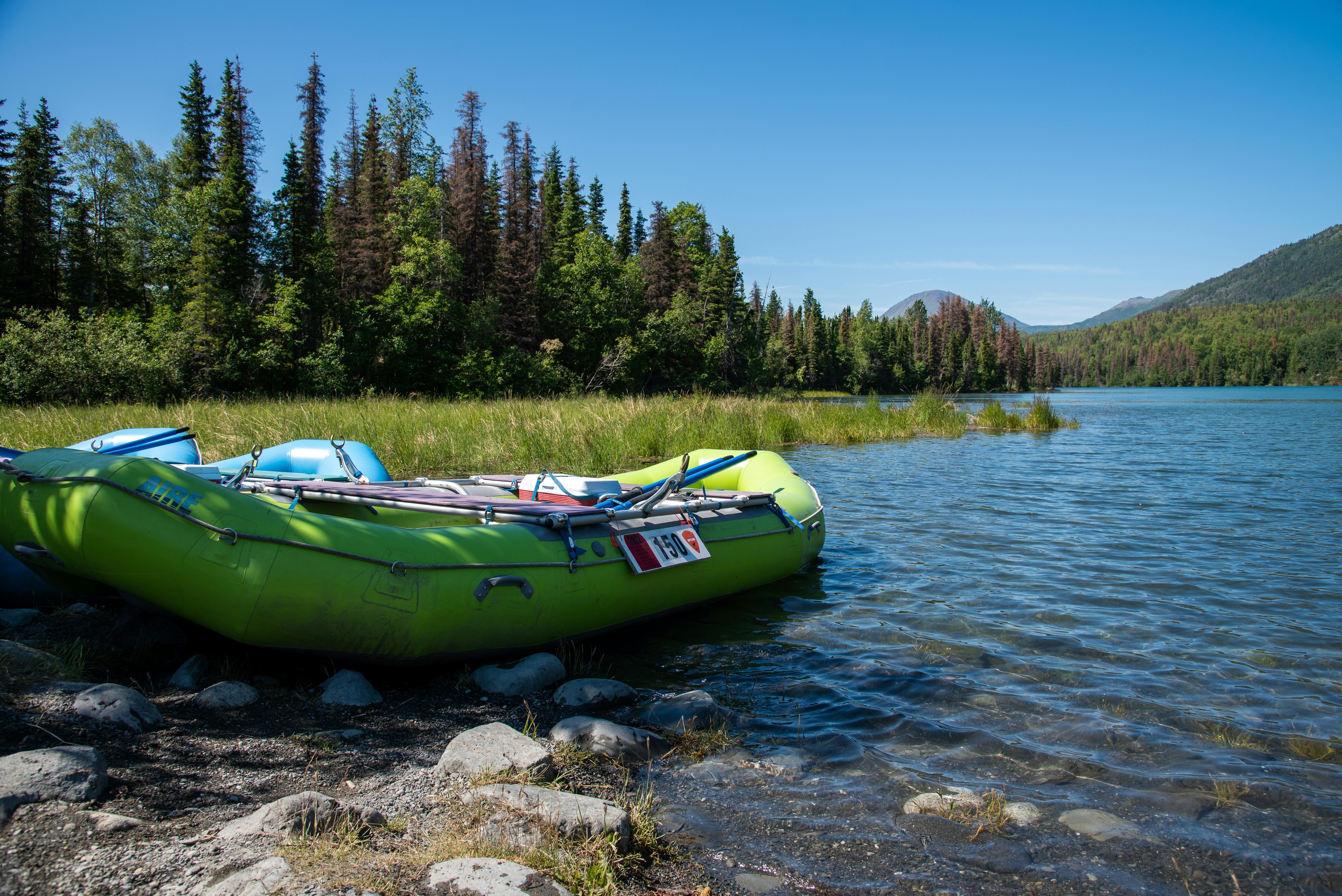 Serene lakeside with a green inflatable raft and forested background under a clear blue sky.