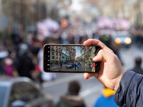 A person captures a bustling Tbilisi street scene on a smartphone, highlighting urban life.