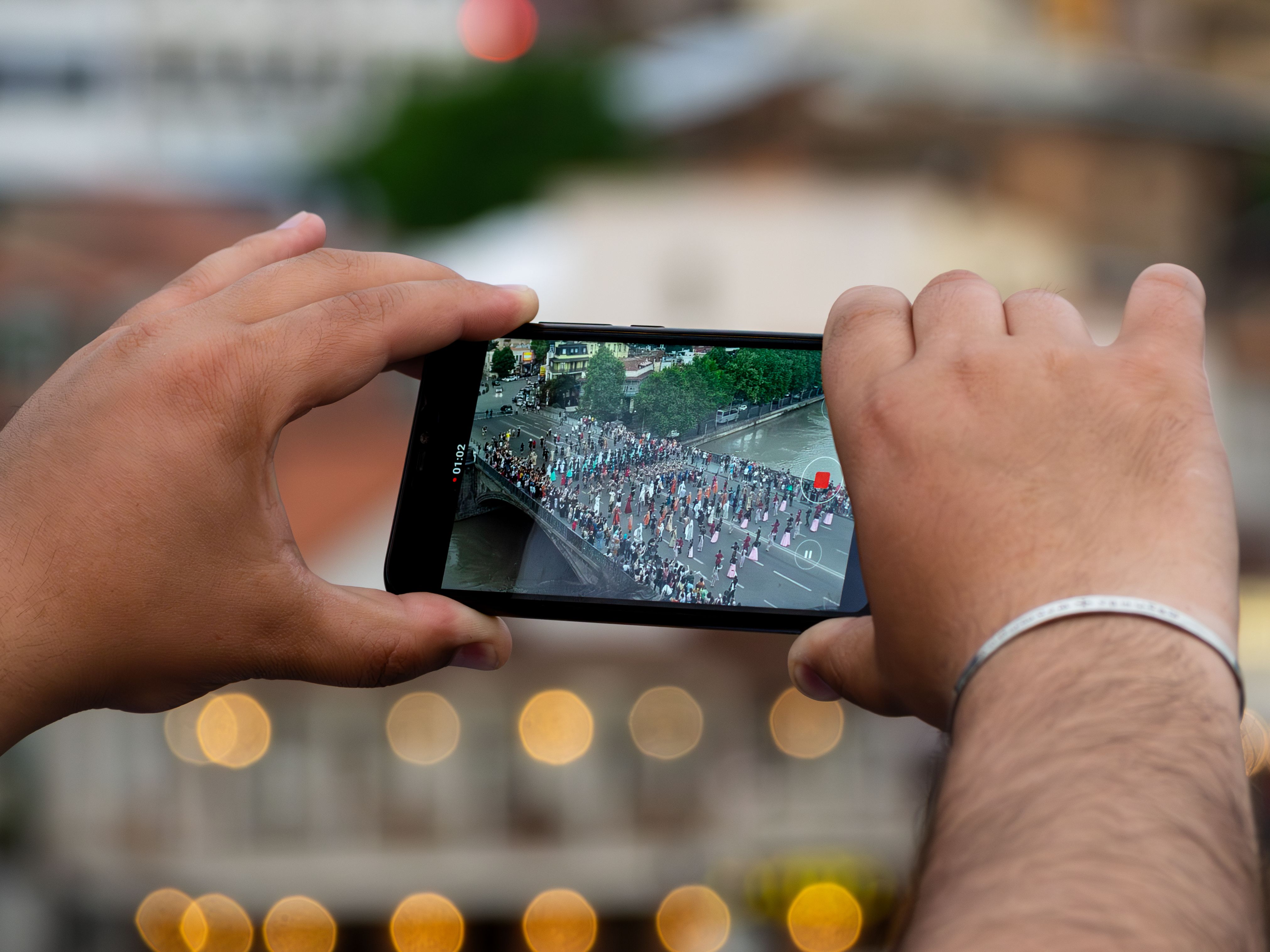Close-up of hands using a smartphone to capture a parade in Tbilisi, Georgia.