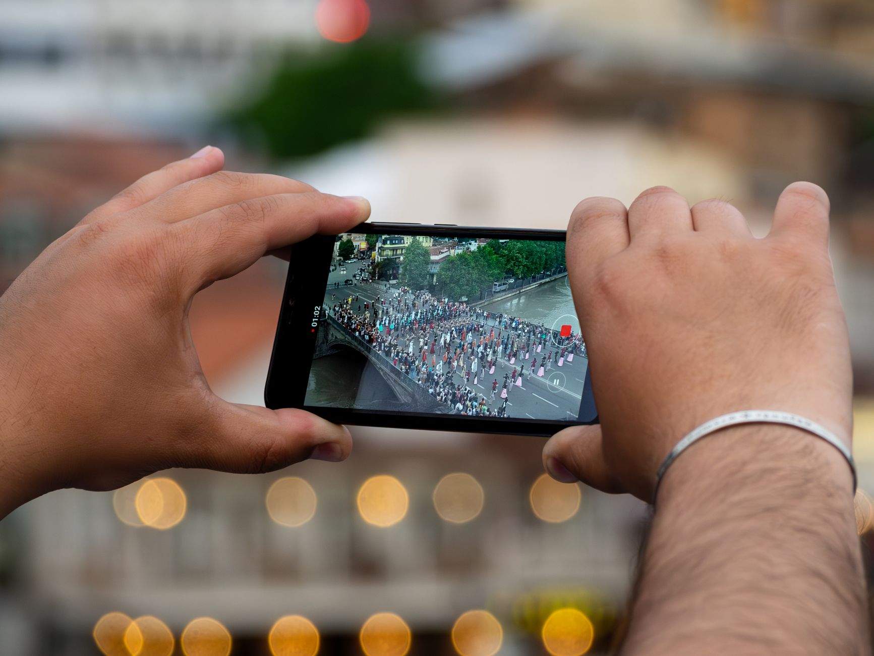 Close-up of hands using a smartphone to capture a parade in Tbilisi, Georgia.