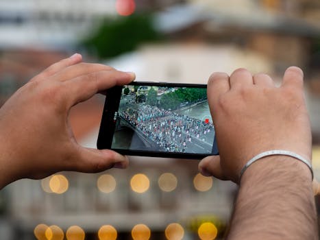 Close-up of hands using a smartphone to capture a parade in Tbilisi, Georgia.