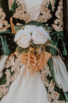 Close-up of a bride's hands holding a white floral bouquet against an ornately embroidered wedding dress.