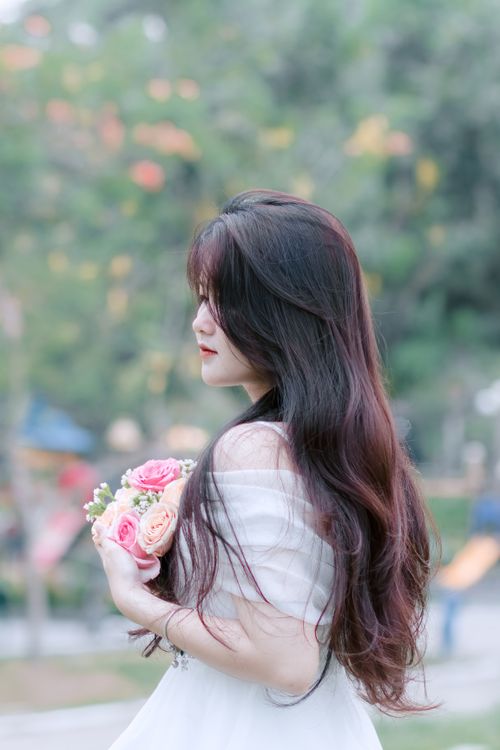 Free Elegant Asian woman in white dress holding rose bouquet outdoors. Stock Photo