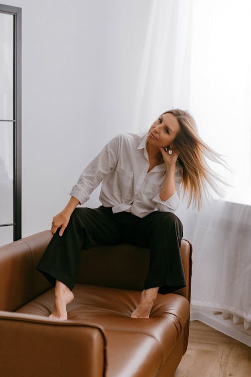 Blonde Woman in White Blouse and Black Wide Trousers Sitting on a Leather Sofa