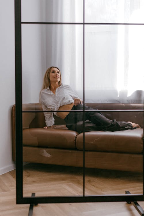 Blonde Woman in White Blouse and Black Pants Posing on a Leather Sofa