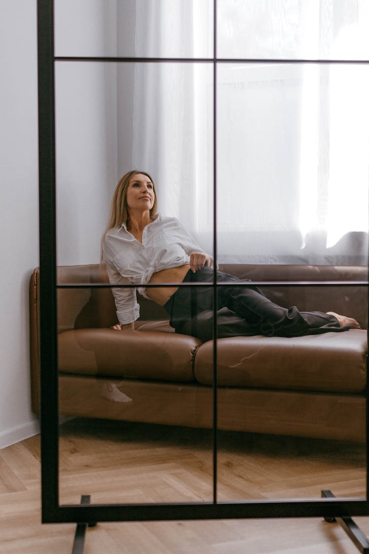 Blonde Woman In White Blouse And Black Pants Posing On A Leather Sofa