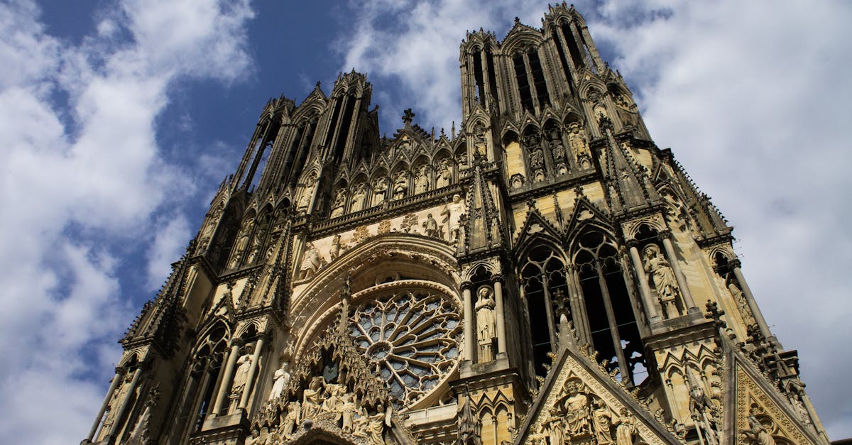 Low angle shot of Reims Cathedral showcasing Gothic architecture against blue sky.