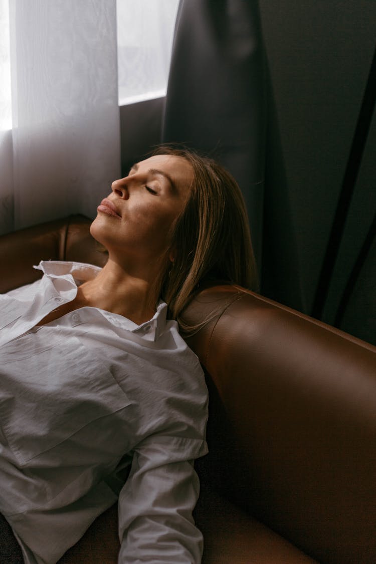 Blonde Woman In White Blouse Lying With Her Eyes Closed On A Leather Sofa