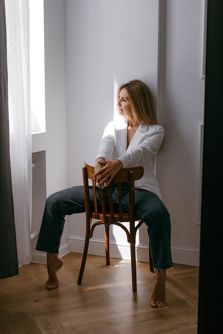 Woman In White Blazer And Jeans Straddling A Chair