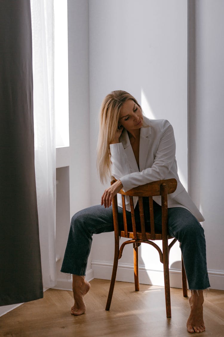 Blonde Woman In White Elegant Blazer Straddling A Wooden Chair