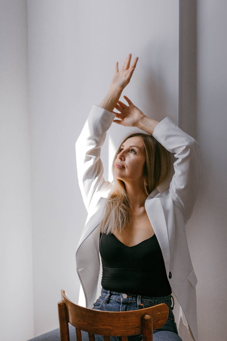 Blonde Woman In White Blazer Sitting Straddling A Chair