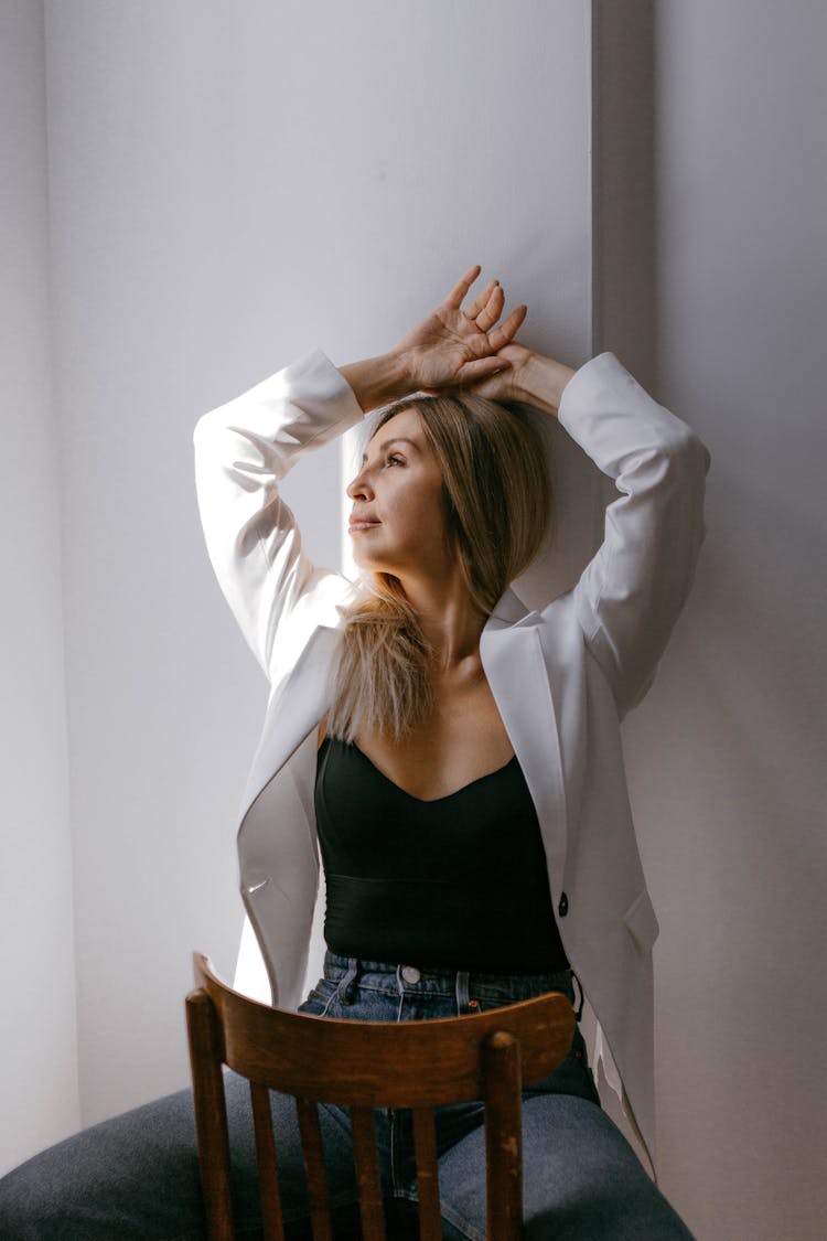 Woman In White Blazer And Black Body Suit Posing On A Chair