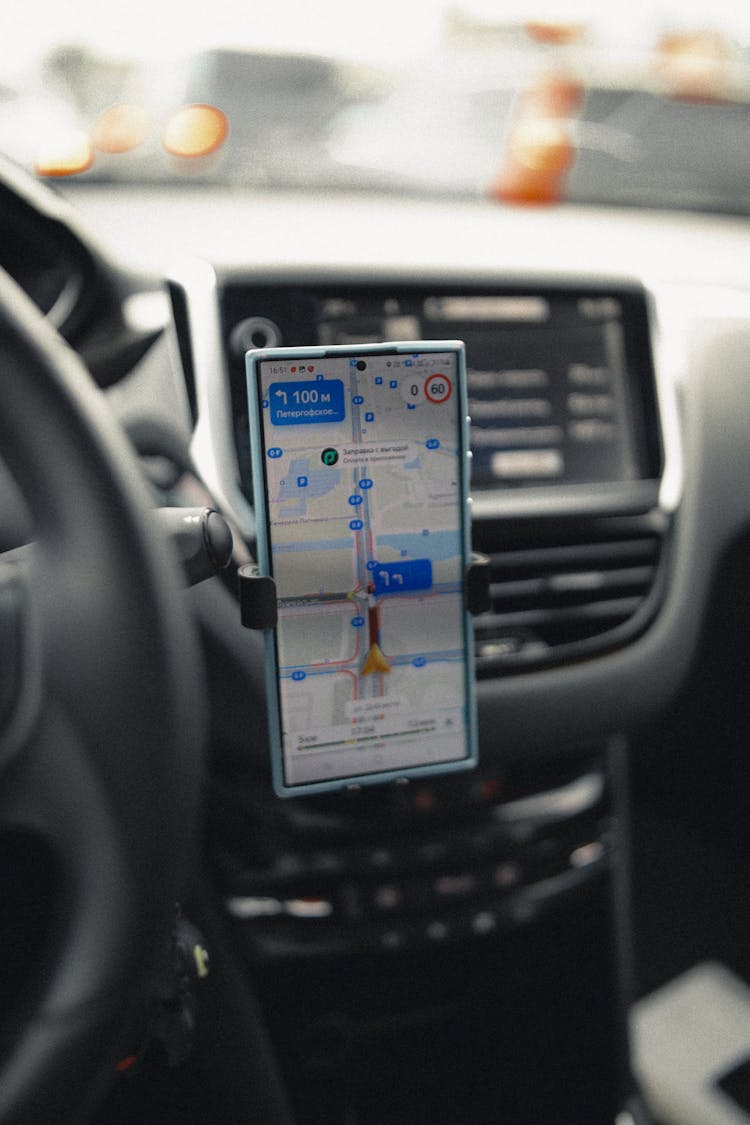 A Smartphone With Displayed Directions Attached Next To The Steering Wheel In A Car 