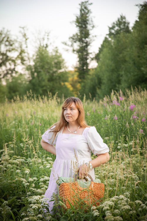 Woman with Basket Standing among Flowers on Meadow