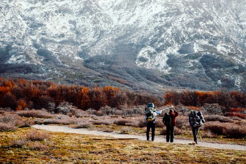 Free Three hikers explore autumn landscapes in El Chalten, Argentina, with snow-capped mountains and vibrant foliage. Stock Photo
