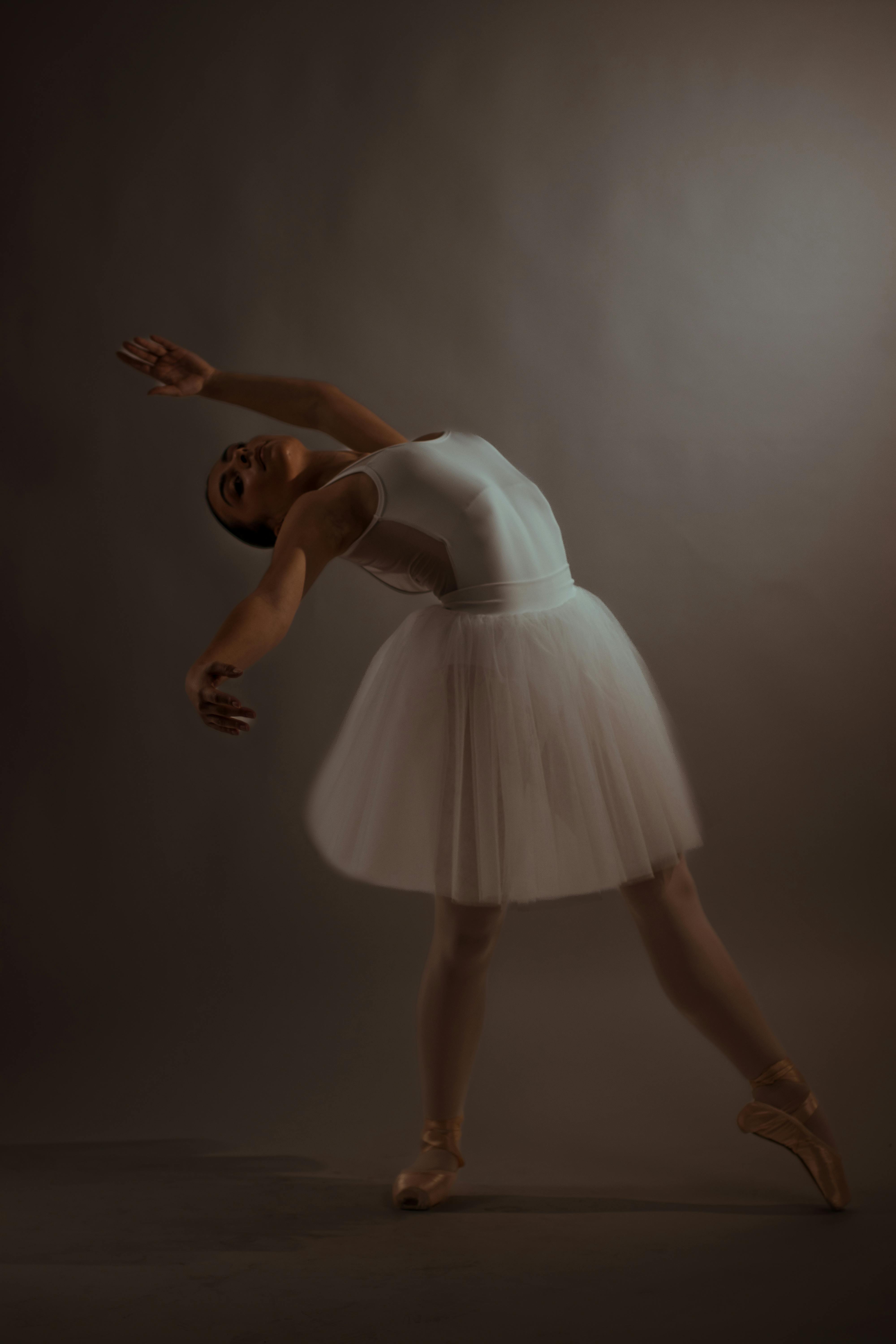 A graceful ballerina performing a delicate dance pose in a white dress, captured in a studio.
