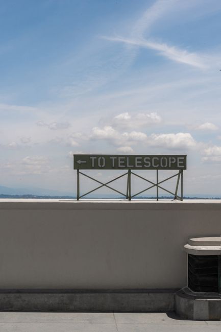 A telescope direction sign at Griffith Observatory under a clear blue sky.