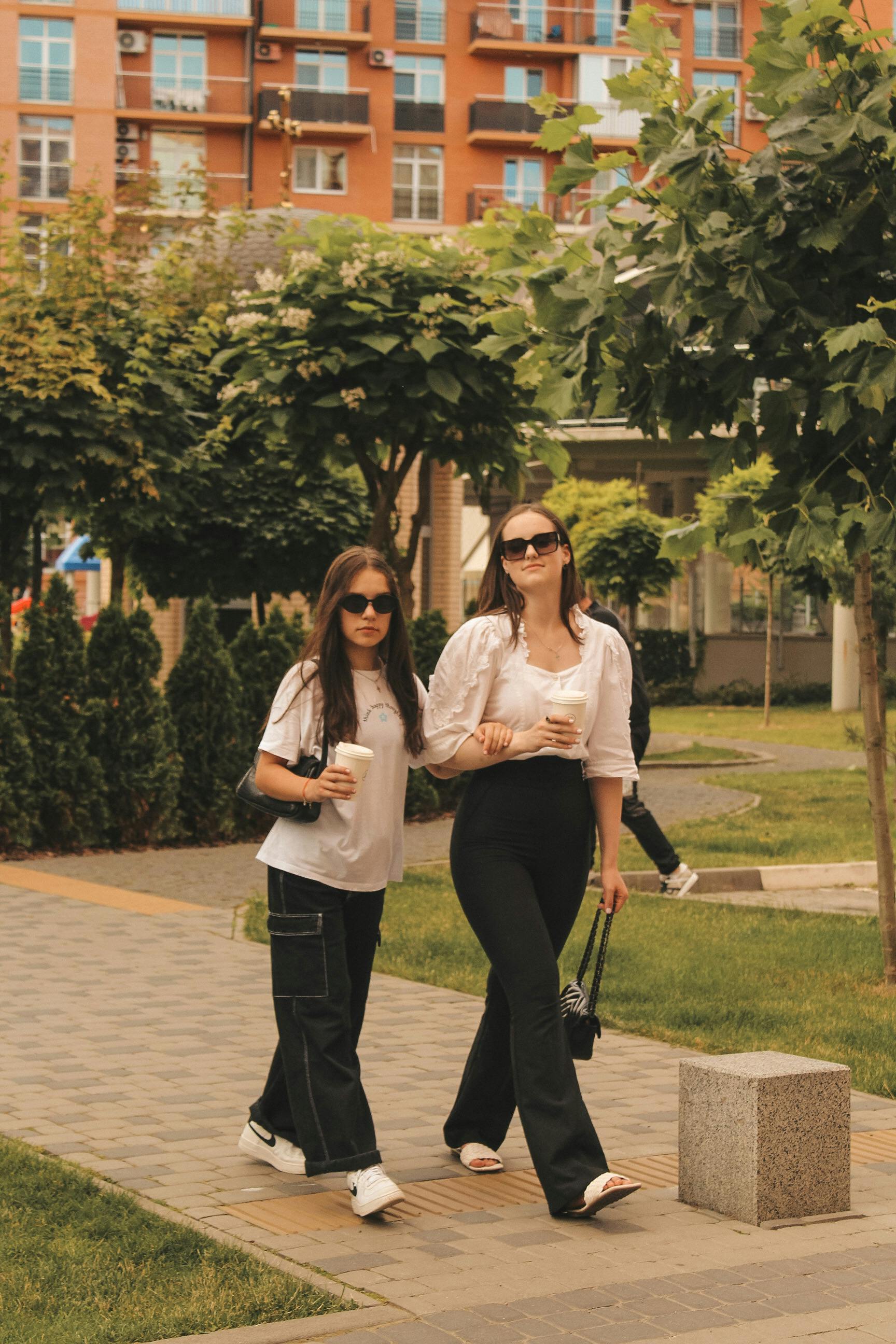 two young women in trendy outfits walking on the pavement in city