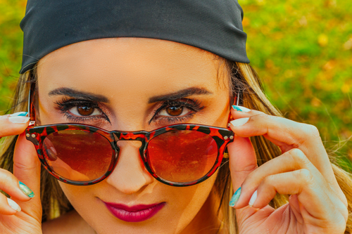 Free Close-up of a fashionable woman adjusting her stylish sunglasses with vibrant background. Stock Photo