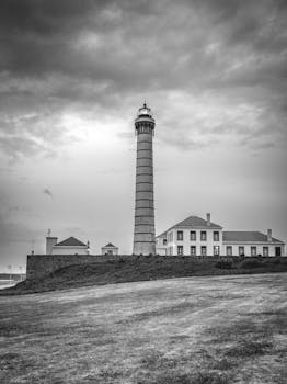 A dramatic black and white photo of the Porto lighthouse under a moody sky at twilight.
