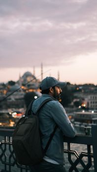 A man stands on Galata Bridge in Istanbul, enjoying a serene sunset view over the cityscape.