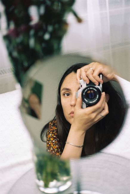 Creative portrait of a woman capturing her reflection with a camera in a mirror.