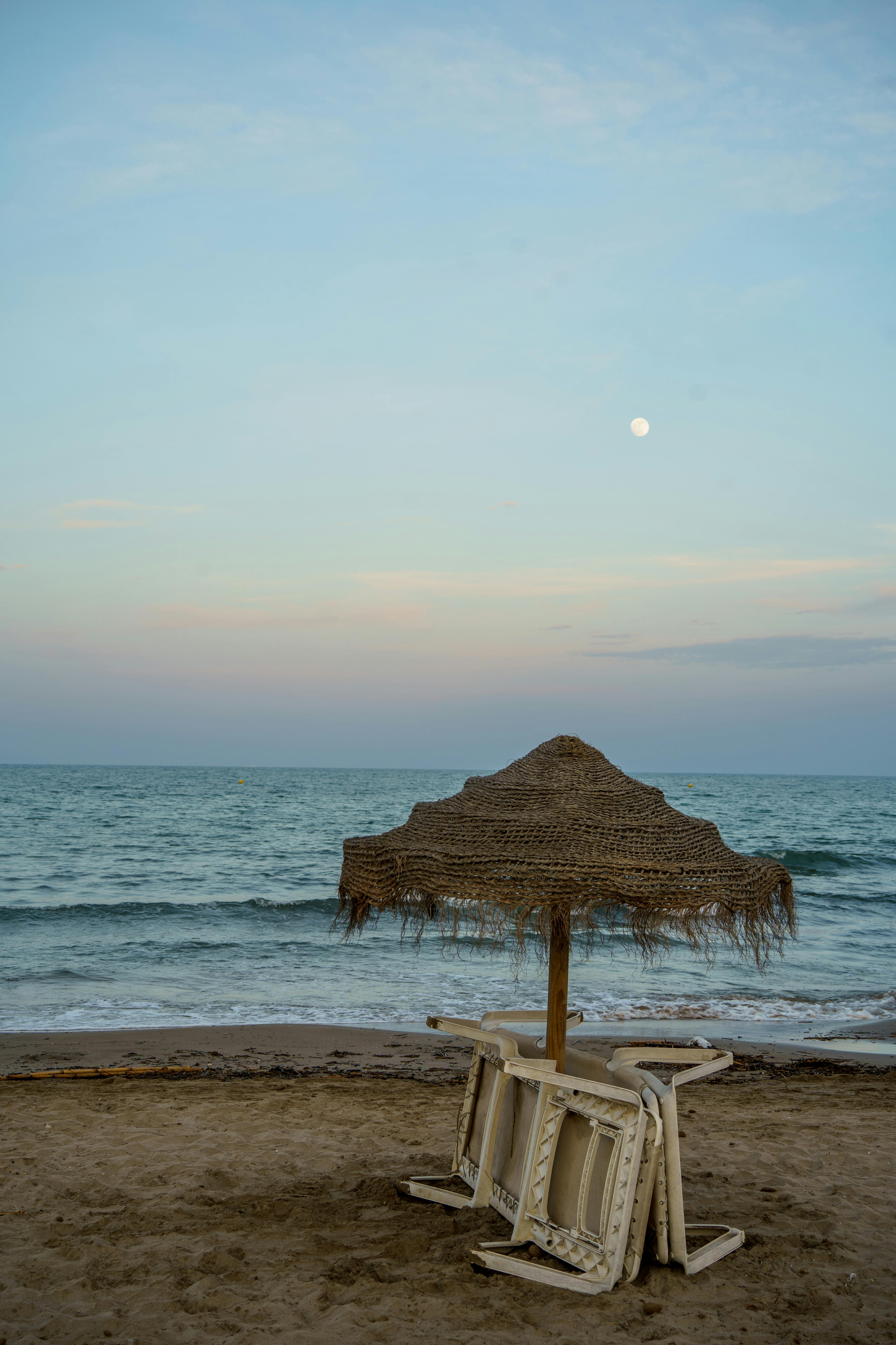 Tranquil seaside view in Valencia, Spain, featuring a straw beach umbrella under a twilight sky.