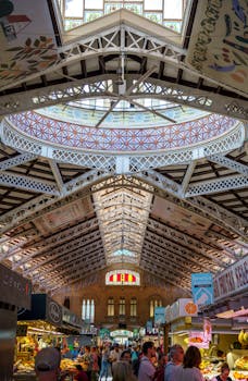 Interior view of the bustling Mercado Central in Valencia, Spain, featuring market stalls and a crowd under the decorative ceiling.