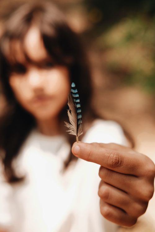Free A young girl holds a small, delicate blue feather outdoors, emphasizing gentle beauty. Stock Photo